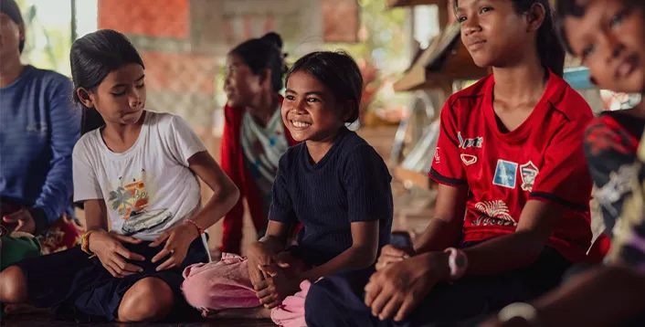 A group of smiling children in Cambodia sitting together on a wooden floor